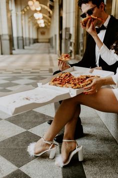 a man and woman sitting on the ground eating pizza