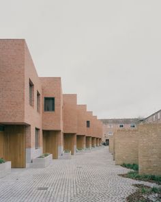 an empty brick walkway between two buildings with wooden doors on each side and another building in the background