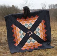 a woman is holding up a quilt on the ground