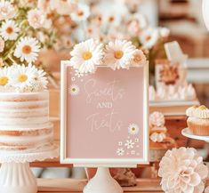 a table topped with cakes and cupcakes covered in frosting next to flowers