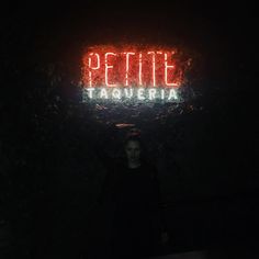 a woman standing in front of a neon sign that reads pettie taqueria