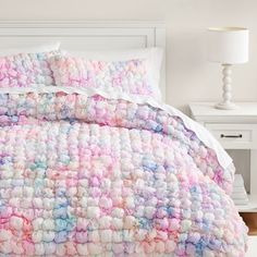 a bed with a white headboard and pink, blue, and green crocheted bedspread