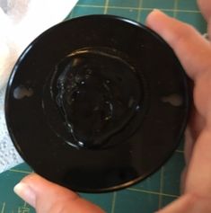 a person holding a black object on top of a green cutting board with white paper