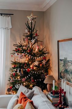 a decorated christmas tree in the corner of a living room with white couches and pillows