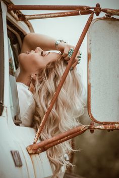 a woman with long blonde hair leaning out the window of an old white truck and looking into the distance