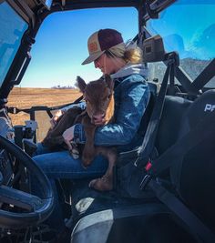 a woman sitting in the driver's seat of a tractor holding a baby cow