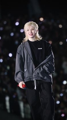 a woman standing on top of a stage wearing black pants and a black jacket with white lettering