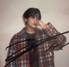 a young man making the peace sign with his hand while standing in front of a white wall