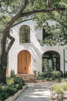 a white house with a wooden door and steps leading up to the front entrance that is surrounded by trees