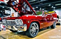 an old red car with its hood open in a showroom filled with people looking at it