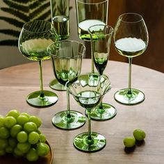 there are many wine glasses on the table with green grapes in front of them and one is empty