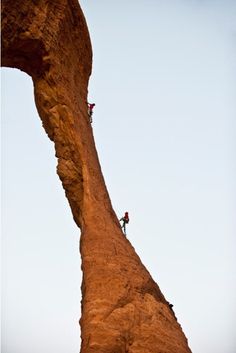 two climbers climbing up the side of a large rock formation, against a blue sky