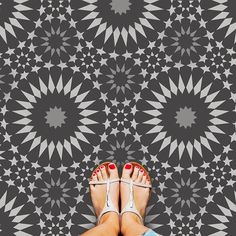 a woman's feet with red nail polish standing in front of a black and white pattern