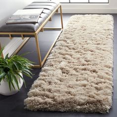 a white rug is on the floor next to a bench and potted plant in front of a window