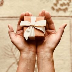 two hands holding a small gift box with a white bow