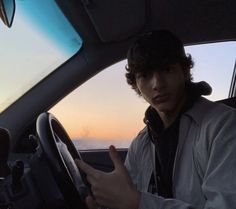 a man sitting in the driver's seat of a car with his hand on the steering wheel