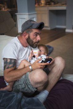 a man holding a baby while sitting on top of a bed