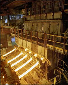 the inside of a factory with lots of steel being lit up by bright yellow lights