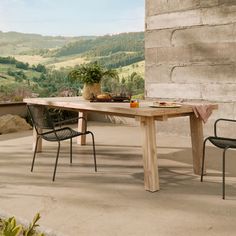 a wooden table sitting on top of a patio next to two chairs and a potted plant