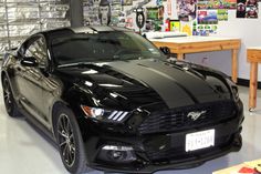 a black mustang parked in a garage next to a wooden table and wall with pictures on it