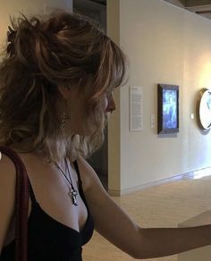 a woman in a black dress looking at paintings on the wall and holding her hand out