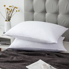 two white pillows sitting on top of a bed next to a cup and saucer