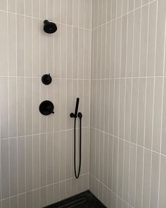 a black and white tiled shower stall with hand held shower head, handset, and soap dispenser