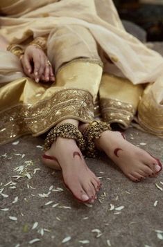 a woman with her bare feet covered in gold and white jewelry sitting on the ground