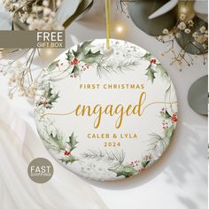 the first christmas engaged ornament is hanging on a table with greenery and lights