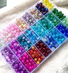 many different colors of beads in a plastic container on a lace tablecloth with white fabric