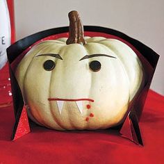 a white pumpkin with an evil face on it's head and black ears, sitting on a red table cloth