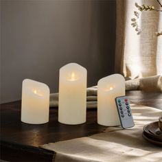 three white candles sitting on top of a table next to a remote control