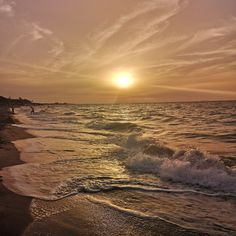 the sun is setting over the ocean with people walking on the beach and in the water