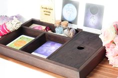 a wooden tray with cards and other items on top of it next to pink flowers