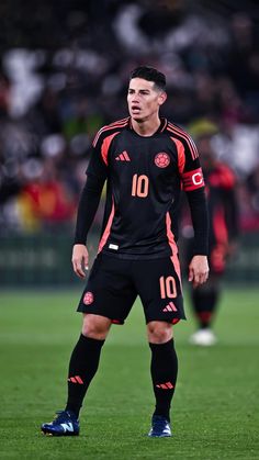 a man standing on top of a soccer field wearing a black uniform and blue shoes