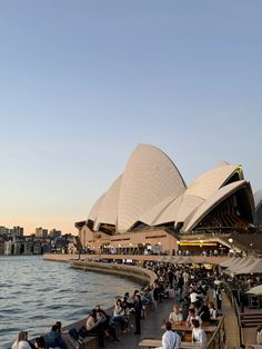 people are sitting on benches near the water in front of the sydney opera house, australia