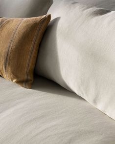 a close up of two pillows on a bed with white sheets and brown pillow cases