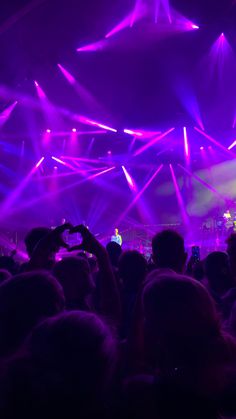 a large group of people at a concert with their hands in the air and lights shining down on them