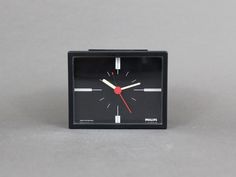 a small black clock with red hands on a gray surface