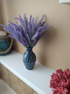 a blue vase with purple flowers sitting on a white shelf next to a red coral