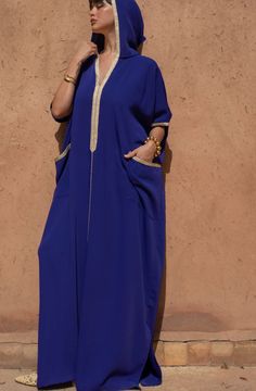 Experience the epitome of Moroccan fashion with our Oversized Crêpe Hooded Jalabiya in a soothing Blue hue. This jalabiya seamlessly combines tradition and modernity, creating a statement piece that's both comfortable and stylish.   Product Details:      Oversized Jalabiya : This jalabiya boasts an oversized fit, providing roominess and comfort for all body types.     Golden "Sfeefa" Details : Adorned with golden "sfeefa" detailing on the neckline, sleeves, and spacious front pockets, this jalab Halston Kaftan, Blue Tunic Thobe For Eid, Oversized Blue Kaftan Tunic, Hooded Kaftan, Moroccan Dresses, Moroccan Clothing, Kaftan Designs, Beautiful Long Dresses, Moroccan Fashion