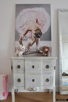 a white dresser sitting next to a wall with a painting on it's side