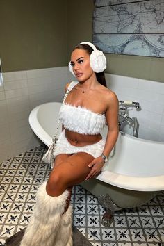 a woman in a bathing suit and headphones sitting on the edge of a bathtub