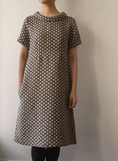 a woman standing in front of a wall wearing a black and white dress with geometric patterns