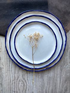 three white plates with blue rims are on a wooden table, one has a flower in the center