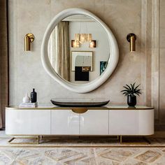 a large round mirror hanging on the wall above a white cabinet with gold trim and drawers