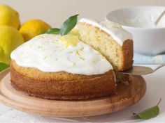 a lemon cake on a wooden plate with a slice cut out and some lemons in the background