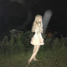 a woman standing in the grass at night wearing a short white dress and holding an umbrella