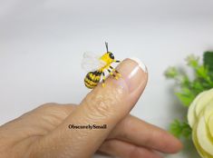 a tiny yellow and black bee sitting on someone's finger next to a flower