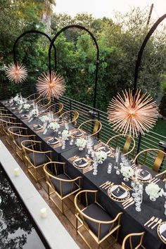 a long table set with black linens and gold chairs, surrounded by greenery